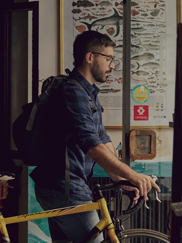 Mattia Garavaglia wyprowadza żółty rower ze swojej księgarni. Nosi okulary i ma na sobie plecak.